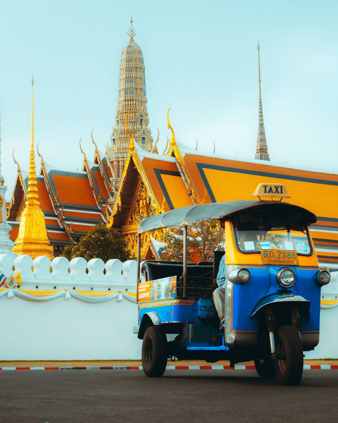A blue and yellow tuk-tuk taxi parked in front of the Grand Palace in Bangkok