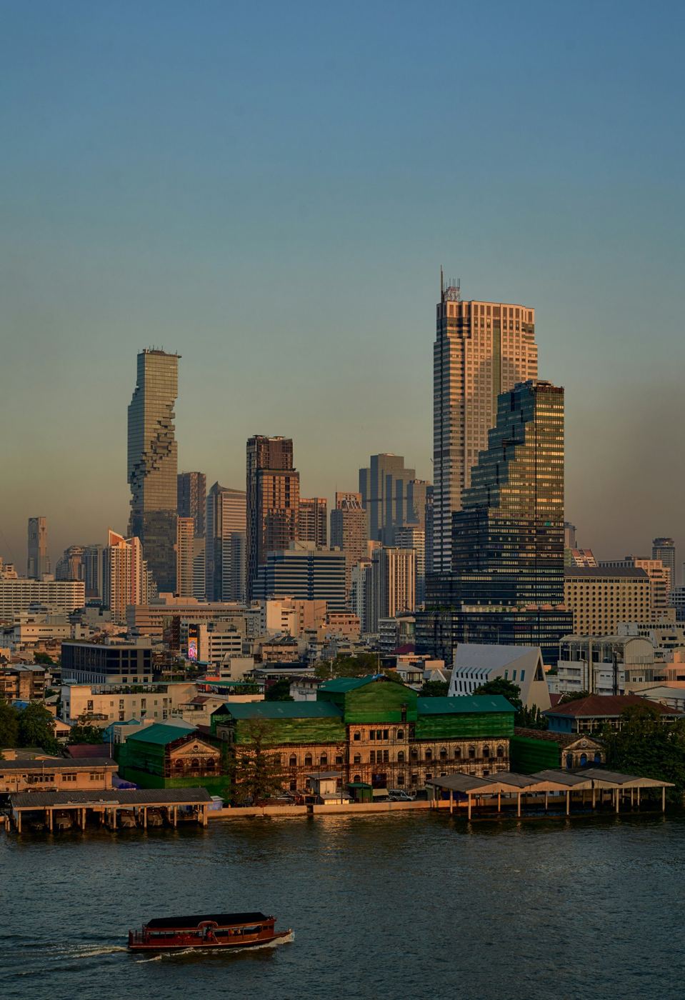 A boat cruising the Chao Phraya River with the Bangkok skyline at sunset
