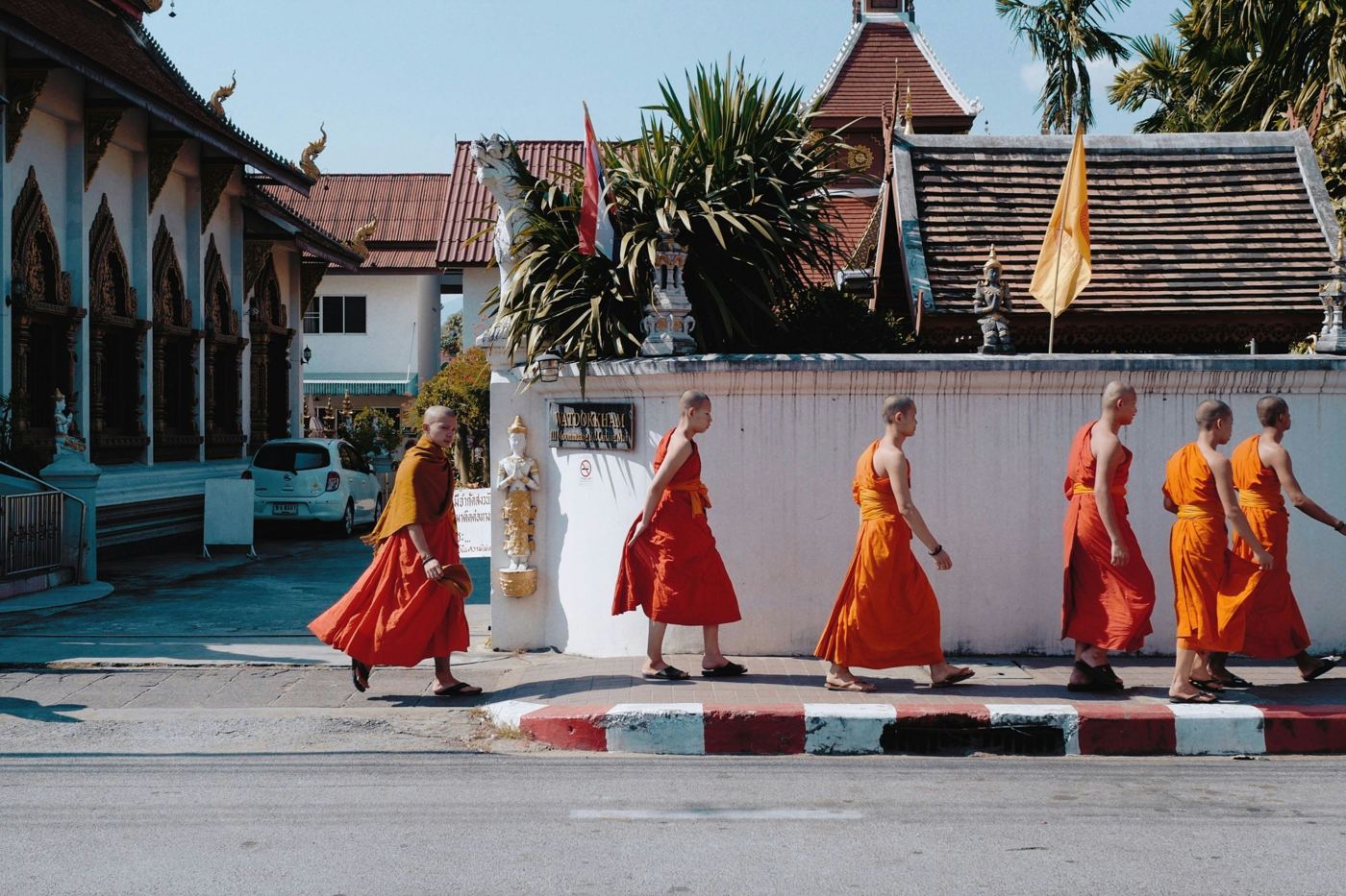 Monks in orange robes walking past a temple wall in Chiang Mai's Old City