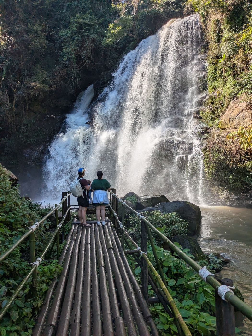 Hikers on a bamboo walkway in front of a waterfall in Doi Inthanon National Park