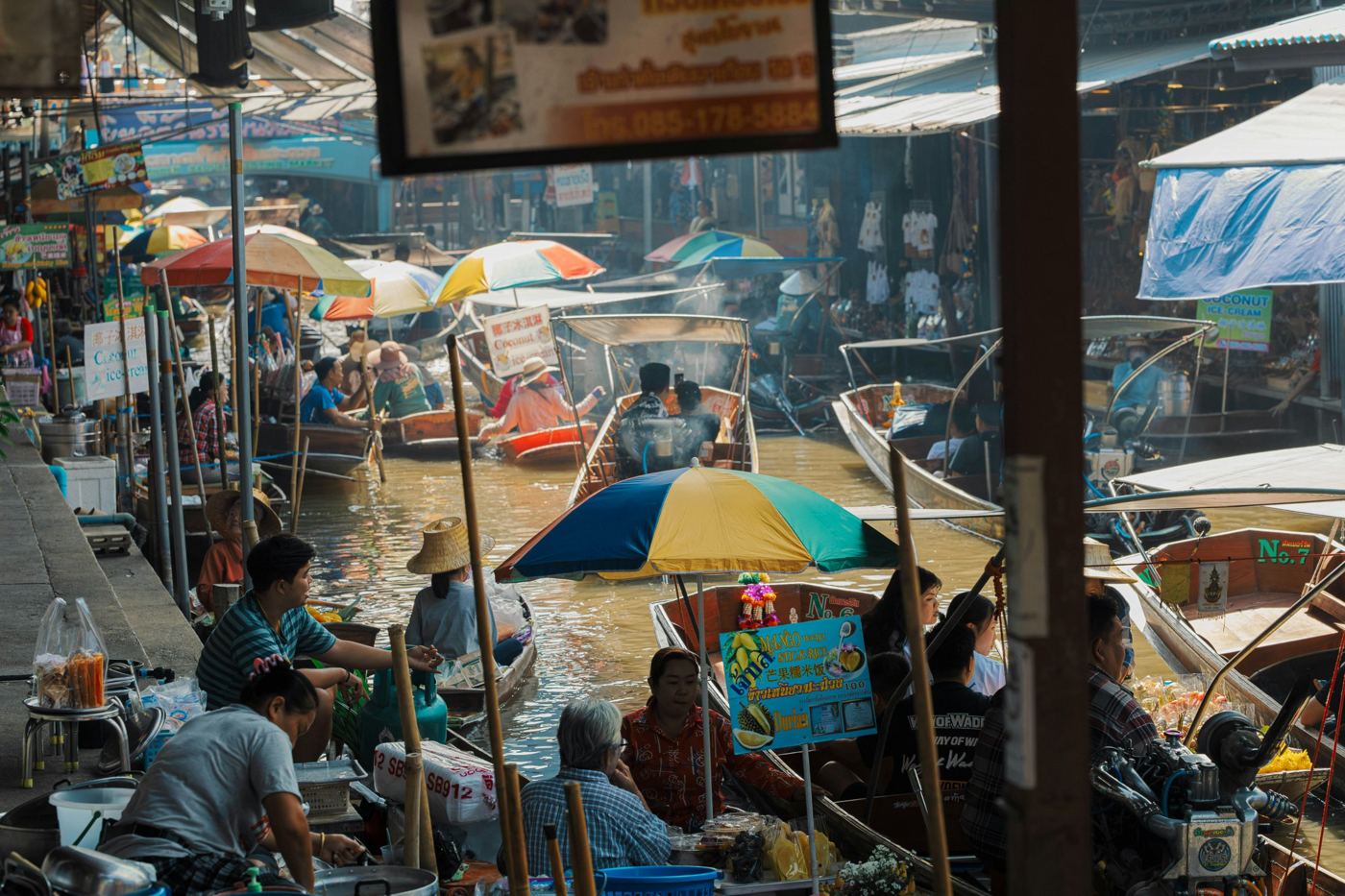 Busy canal at a Thai floating market with colorful umbrellas and wooden boats