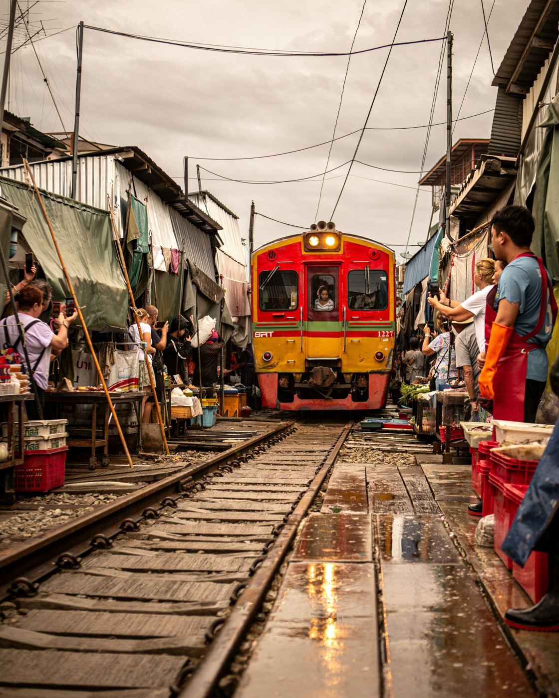 A red and yellow train rolling through the stalls of the Maeklong Railway Market