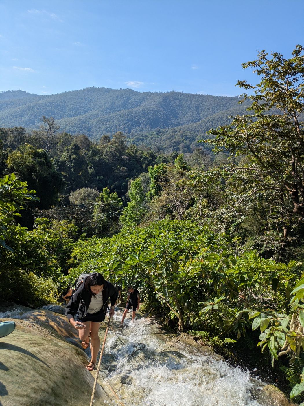 Climbing up the Sticky Waterfall with mountains in the background