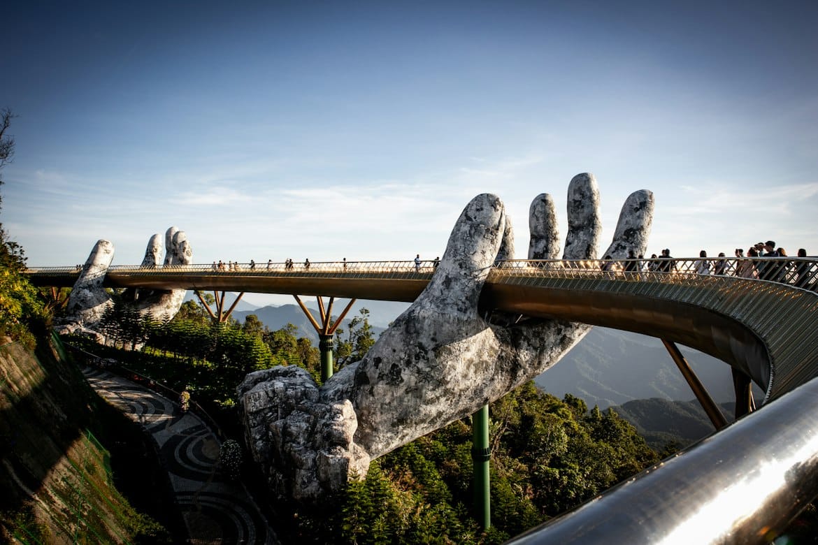 Visitors walking across the Golden Bridge, held up by giant stone hands above the forest