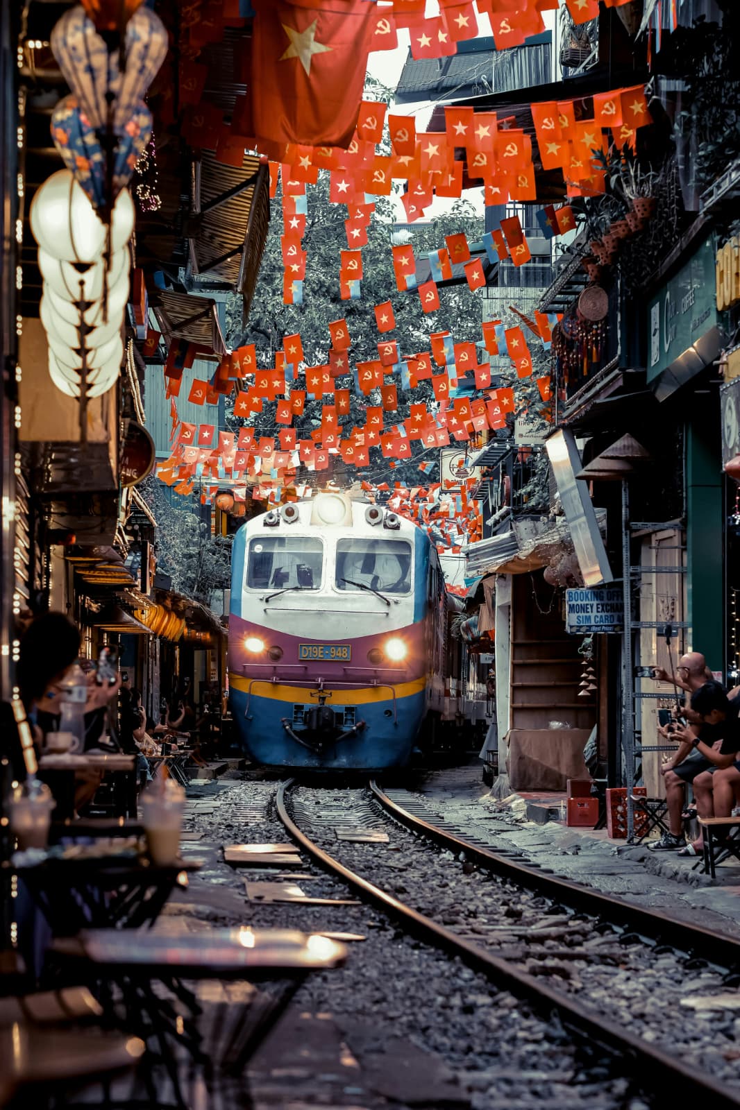 Train coming down Hanoi Train Street beneath strings of red flags