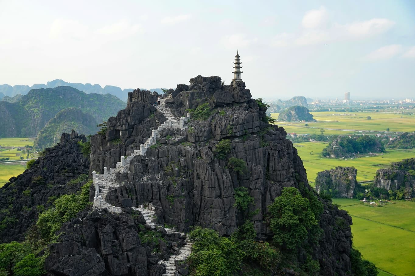 Pagoda on the rocky peak above Mua Cave, with stone steps and rice fields below